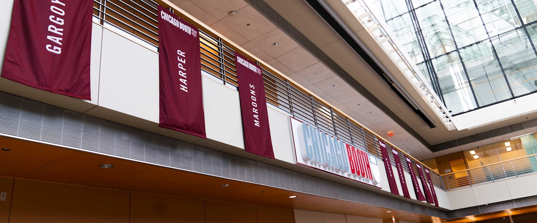 Banners and the "Chicago Booth" sign in the Winter Garden at the Harper Center. The banners read "Gargoyle", "Harper", and "Maroons".