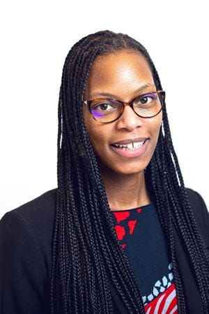Candice, a Black woman with long braids and cat eye glasses, smiles at the camera.