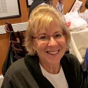 A white woman with bangs and red rimmed glasses smiles at the camera.