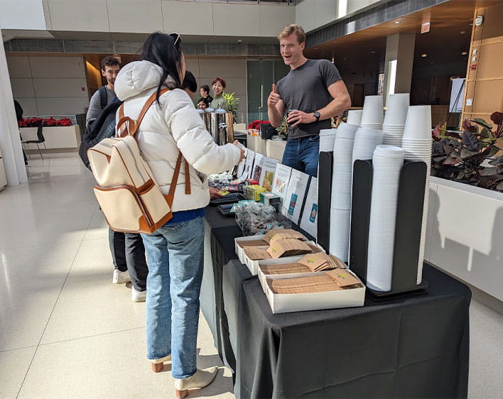 individual from Booth community giving thumbs up while students get free drinks