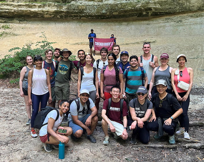 members of Booth outdoors club taking photo together outside with Booth Flag in background held up by two students 