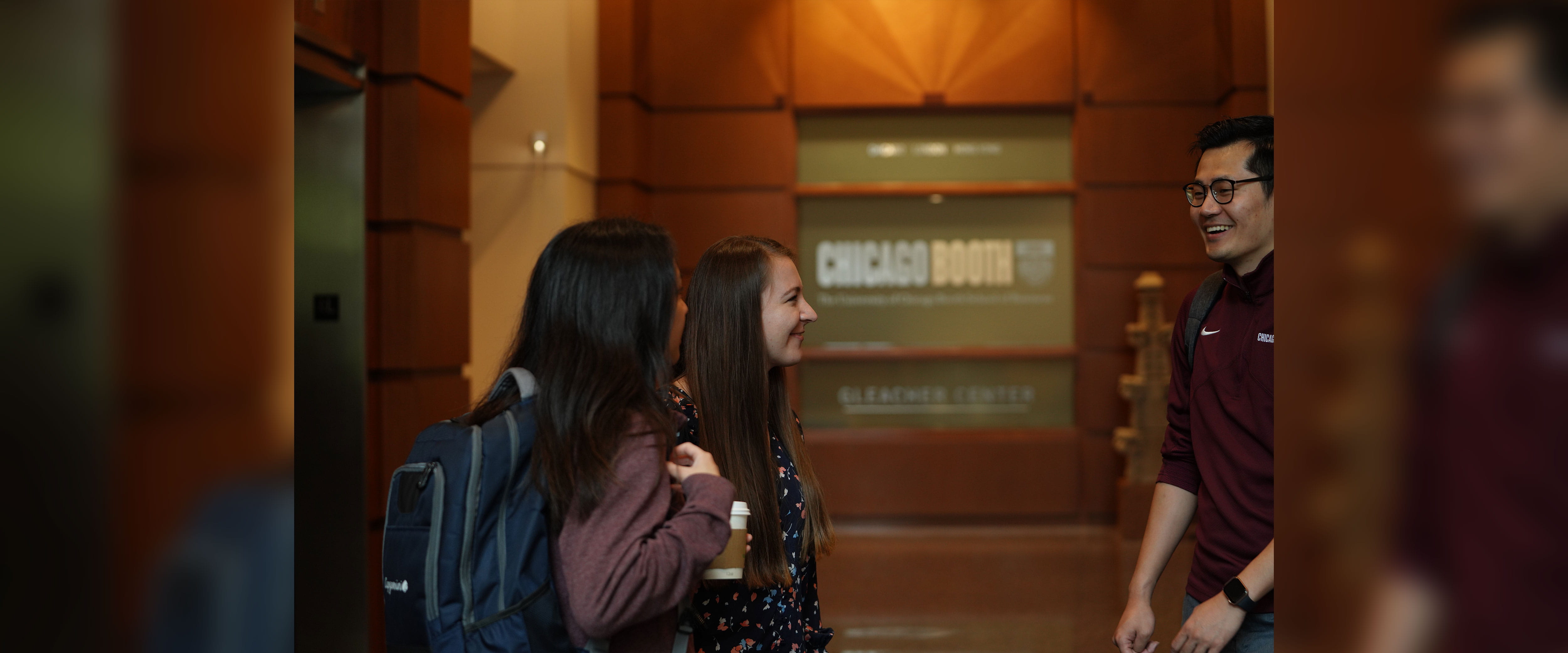three students conversing inside of Gleacher Center lobby