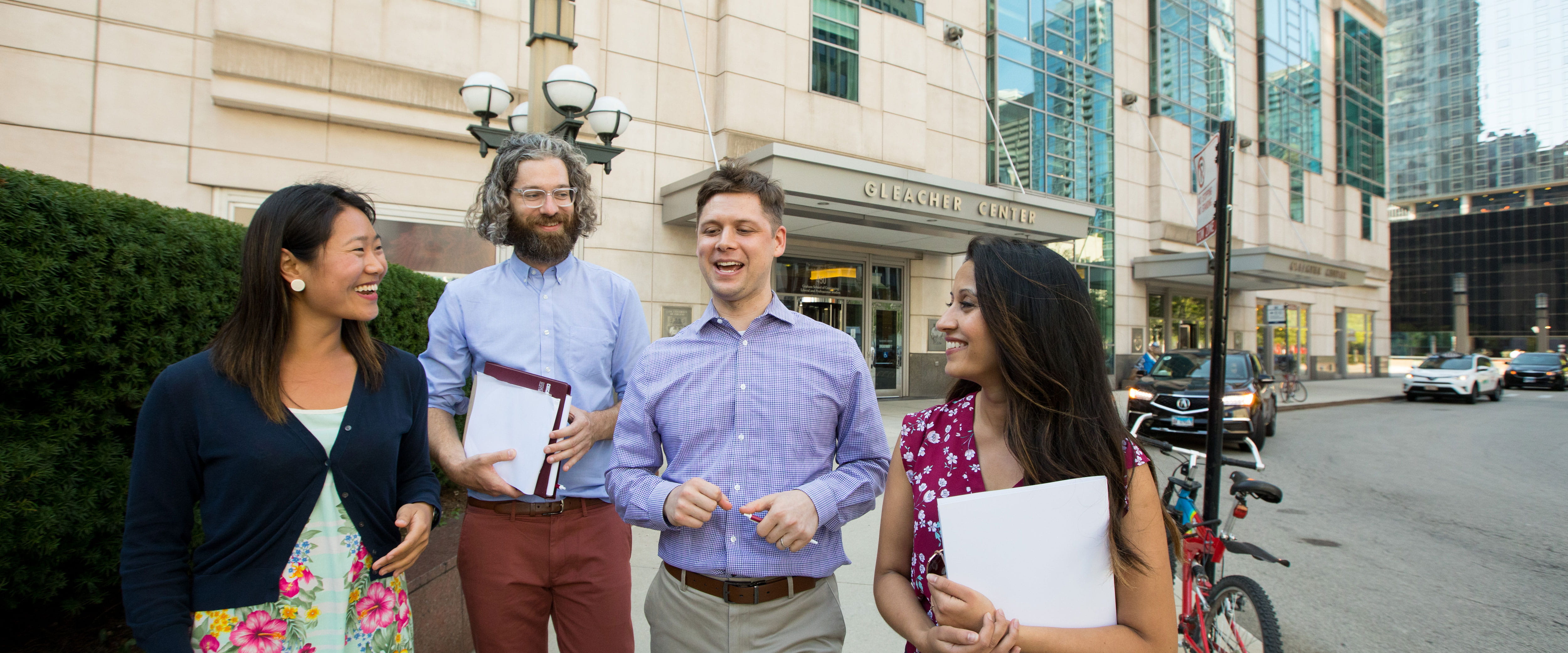 Four students conversing while walking outside of the Gleacher Center
