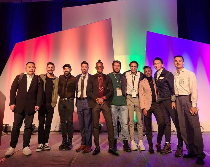10 Boothies smiling in group photo taken indoors with colorful background