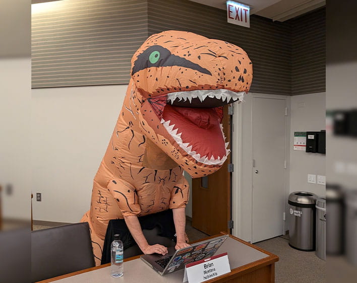 Brian at Chicago Booth in classroom with dinosaur costume on