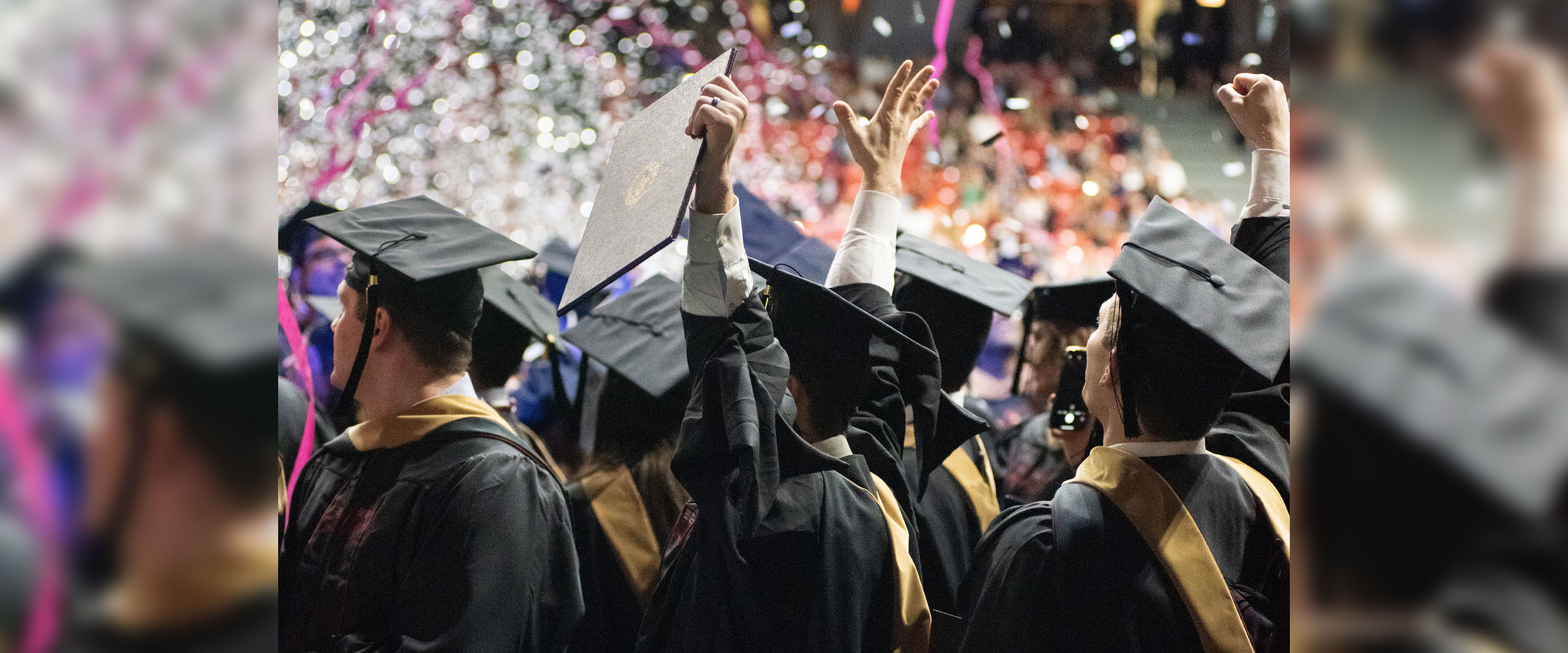 Boothies in cap and gown at graduation showing side profiles with confetti in background