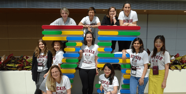 A group of several women students gather pose for a photo around a colorful sculpture of the number 75