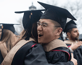 Two Booth graduates embrace in graduation regalia