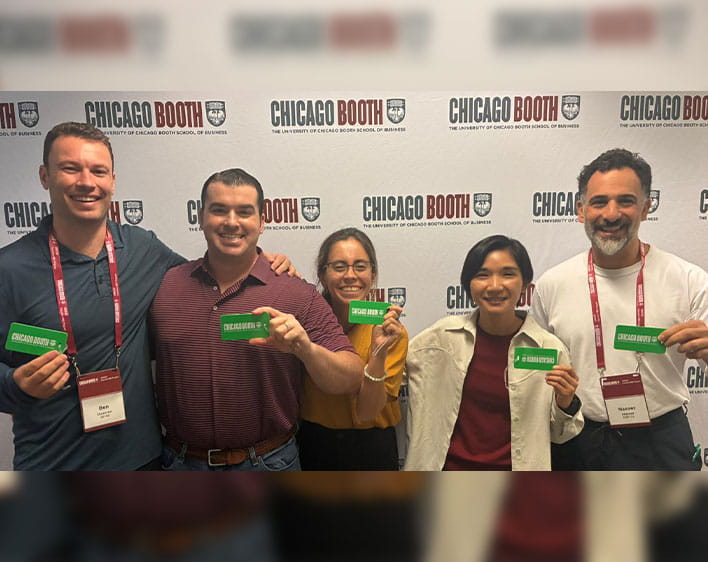 Nasser with four other Booth students smiling in front of Chicago Booth banner with green Chicago Booth tags in their hands