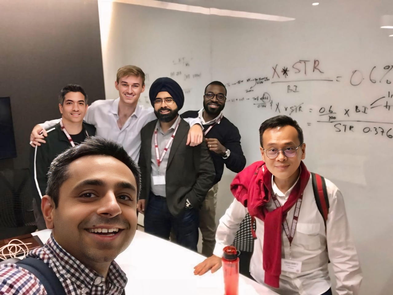 A group of people standing in front of a whiteboard and looking at the camera