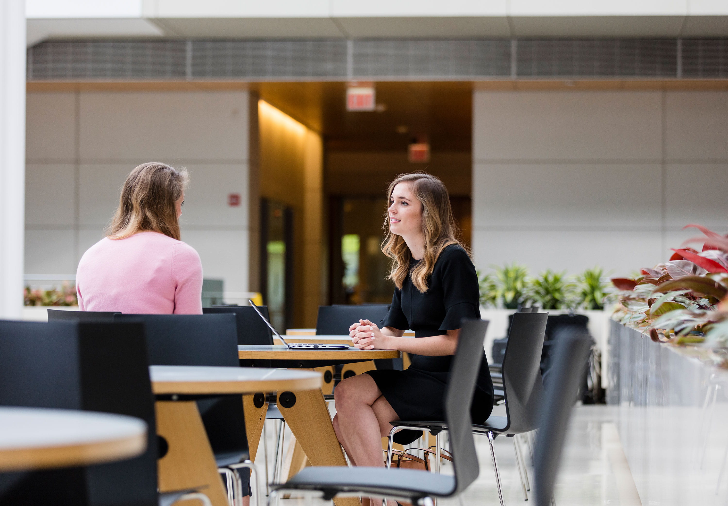 Two female students converse over a laptop in the Harper Center Winter Garden