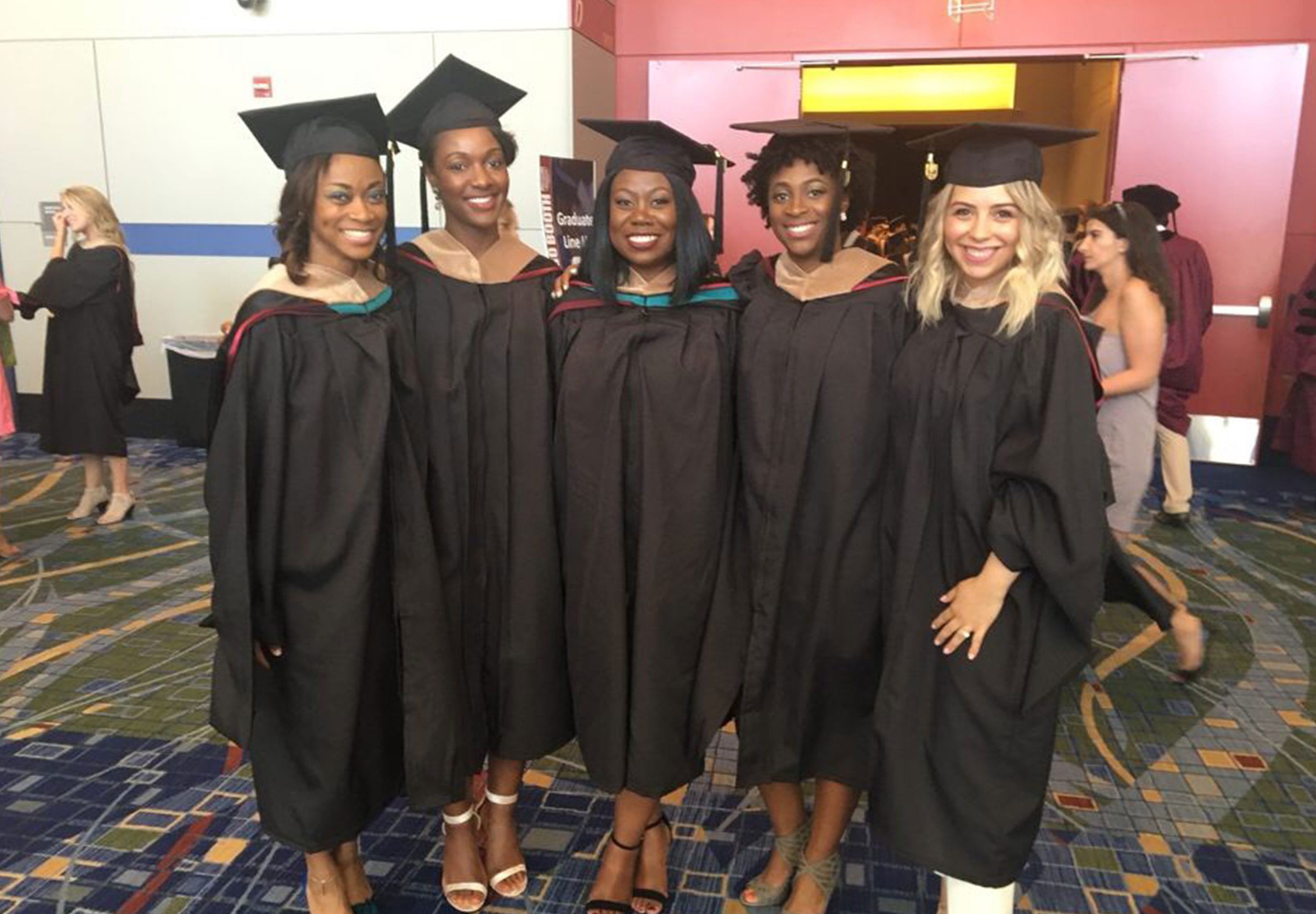 A group of alumnae smile in their caps and gowns