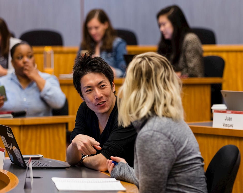 A male student smiling, speaking to a female student in classroom
