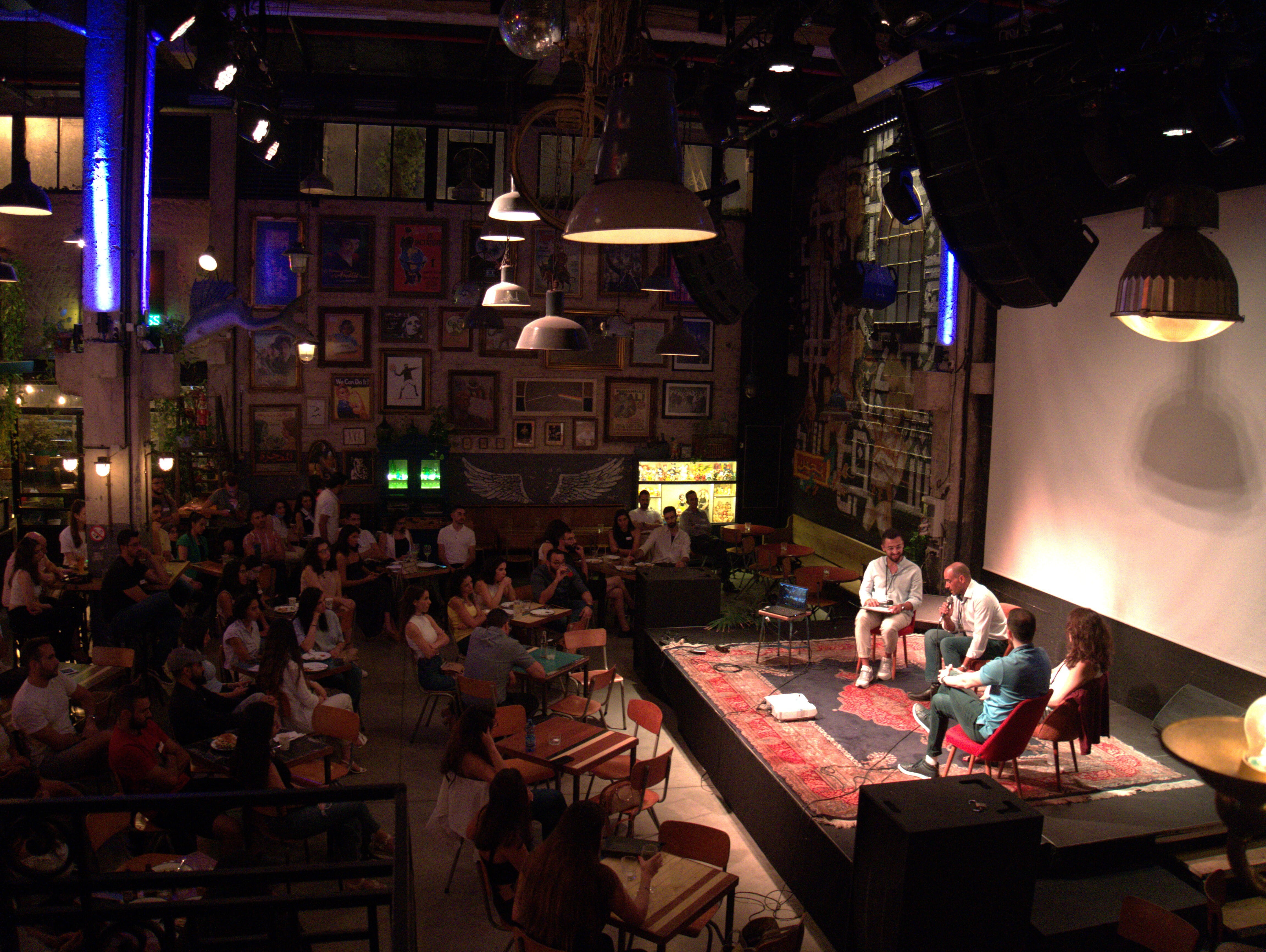 Booth Alum, Amir Akleh on stage for event with audience sitting down at tables around the stage 