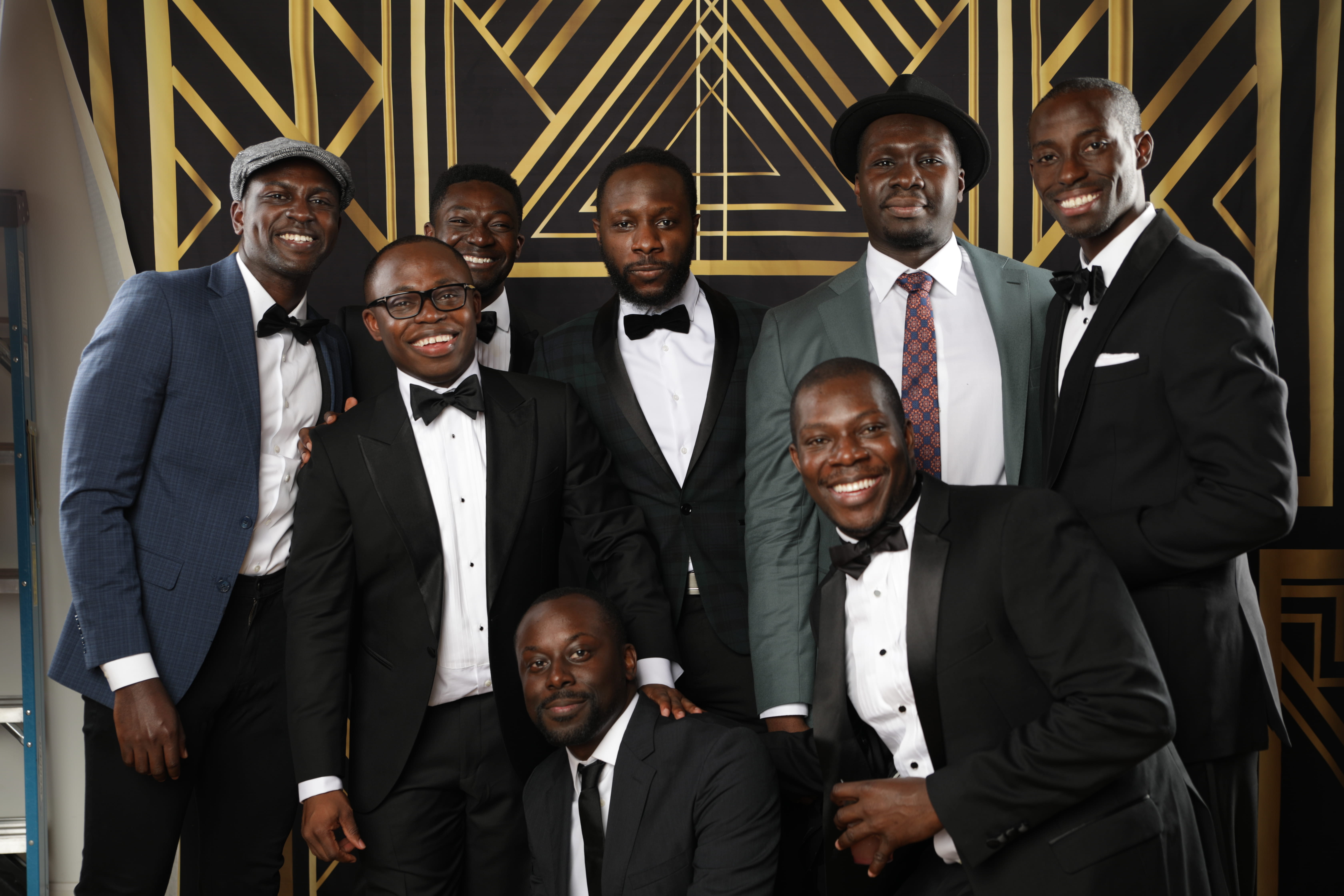 Kwaku Frimpong and other Boothies smiling in suits with gold and black background 