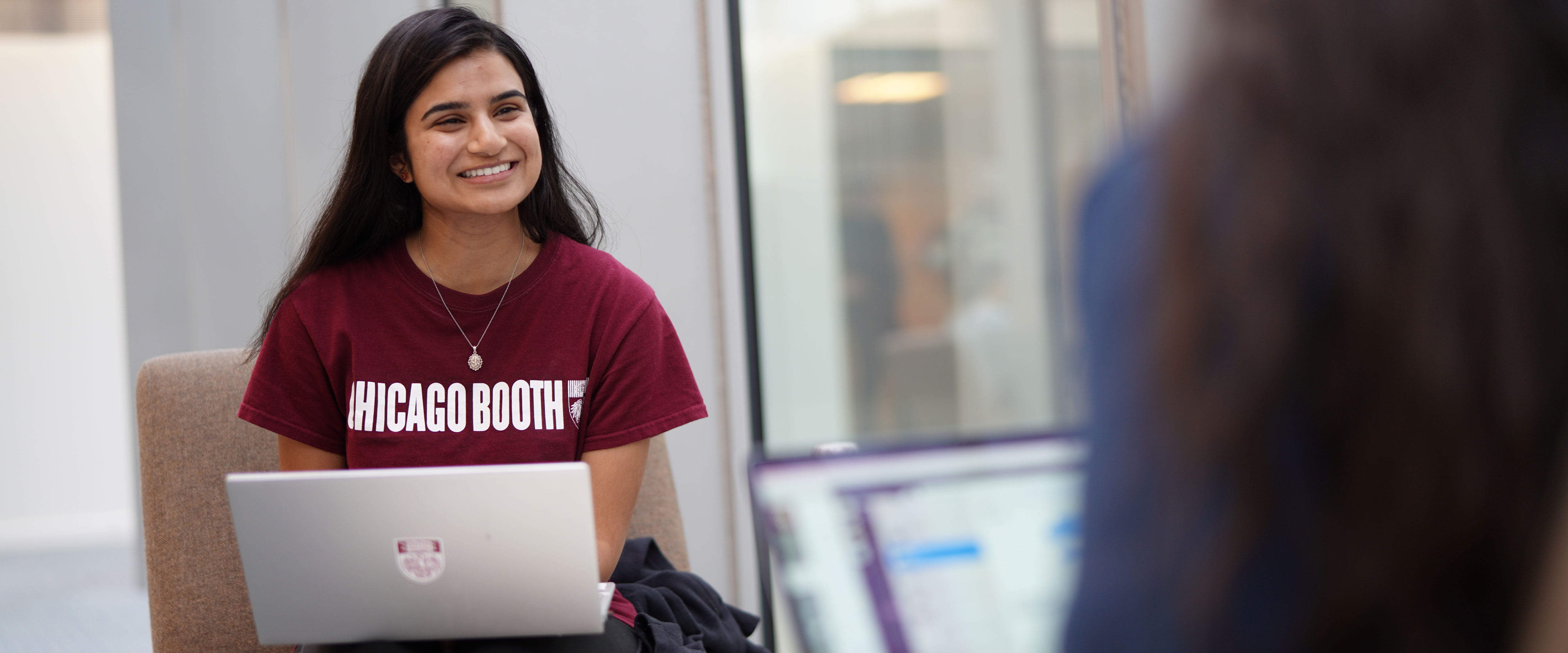 Woman smiling while sitting down with laptop in lap with Chicago Booth t-shirt on