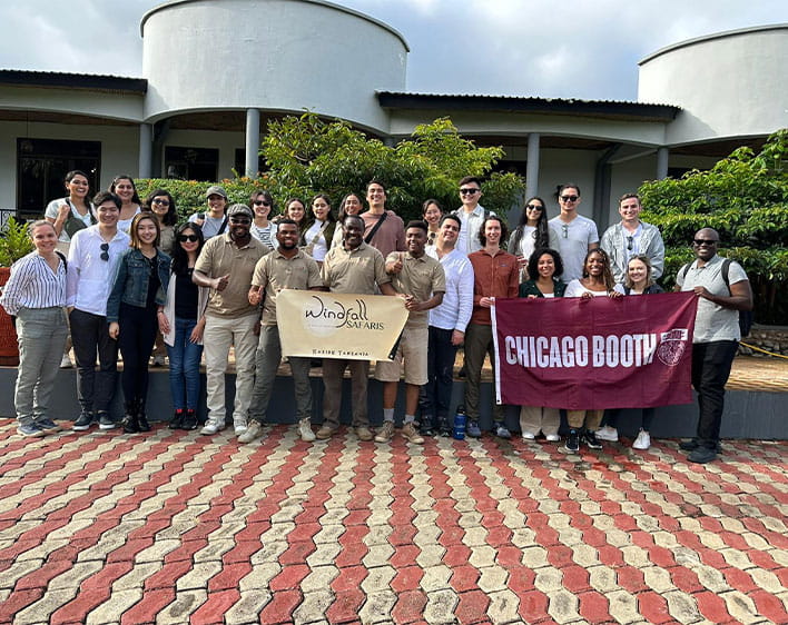 large group of Boothies and tour leaders posing outside with Booth flag and Windfall Safaris flag
