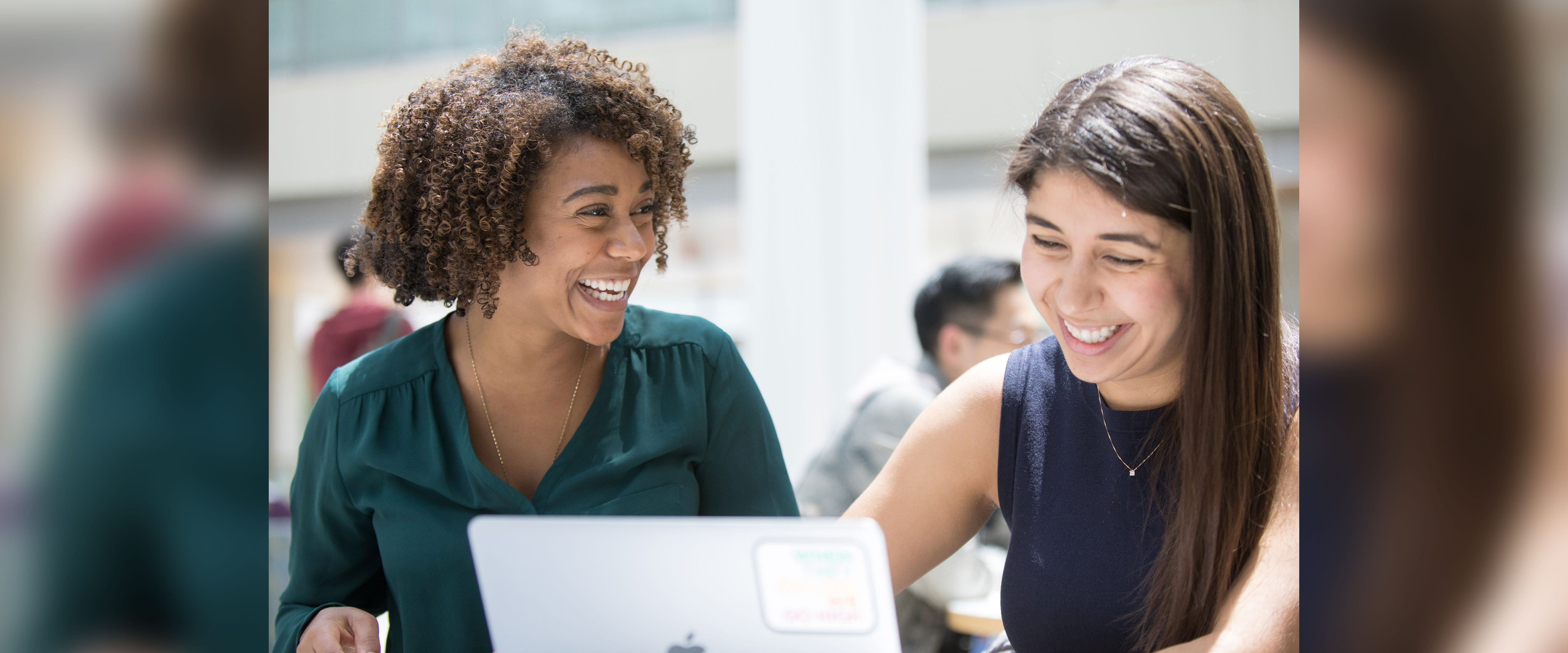 two Boothies smiling while one is looking towards the other and one is looking at their laptop