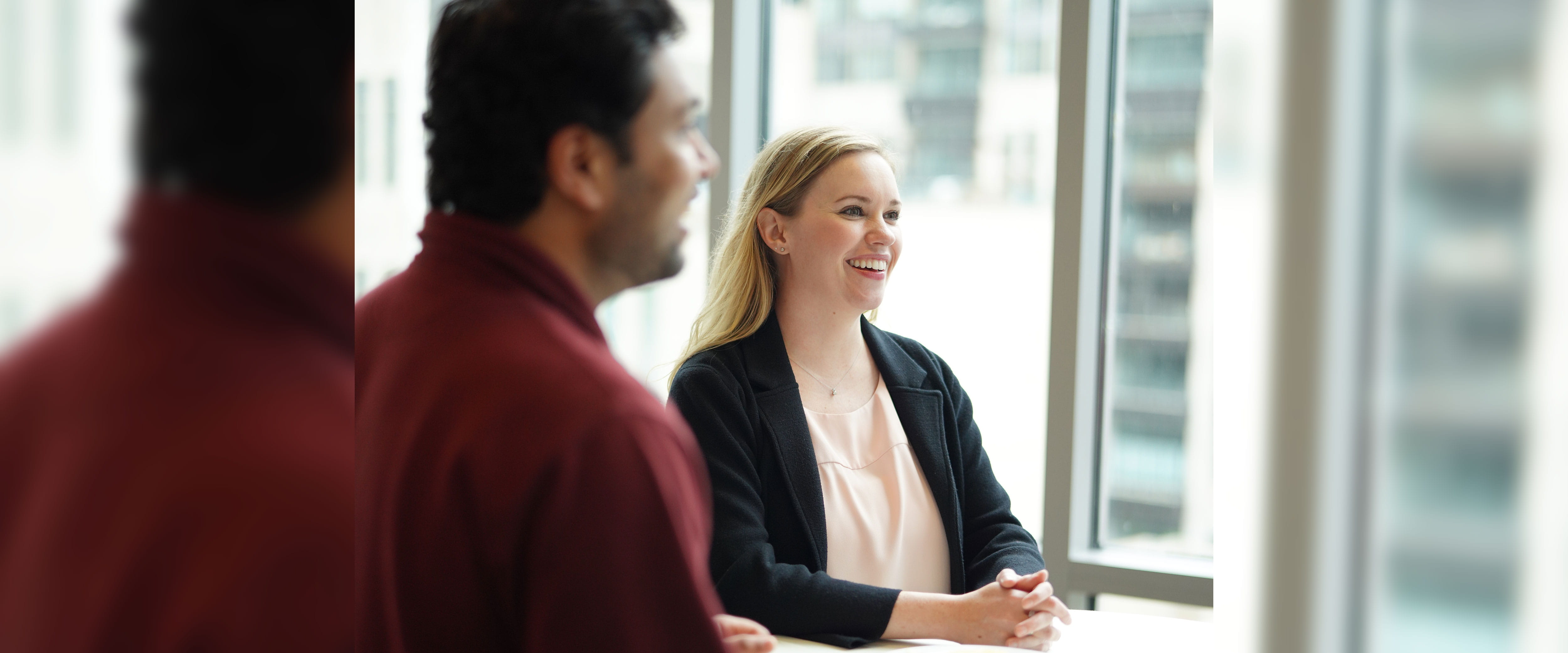 Two Boothies standing at table with one Boothie smiling with hands on table looking forward and the other with back facing camera 