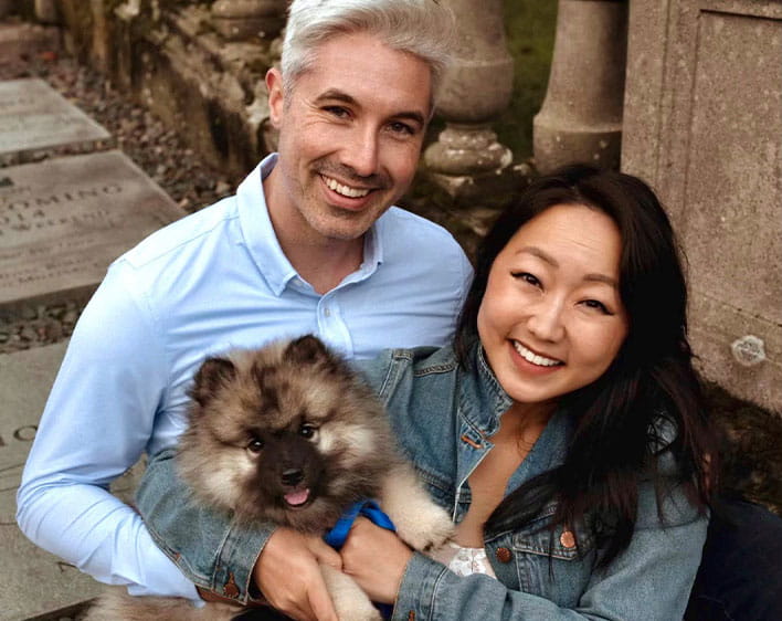 Michelle Kim Cullen sitting down holding dog and smiling next to husband 