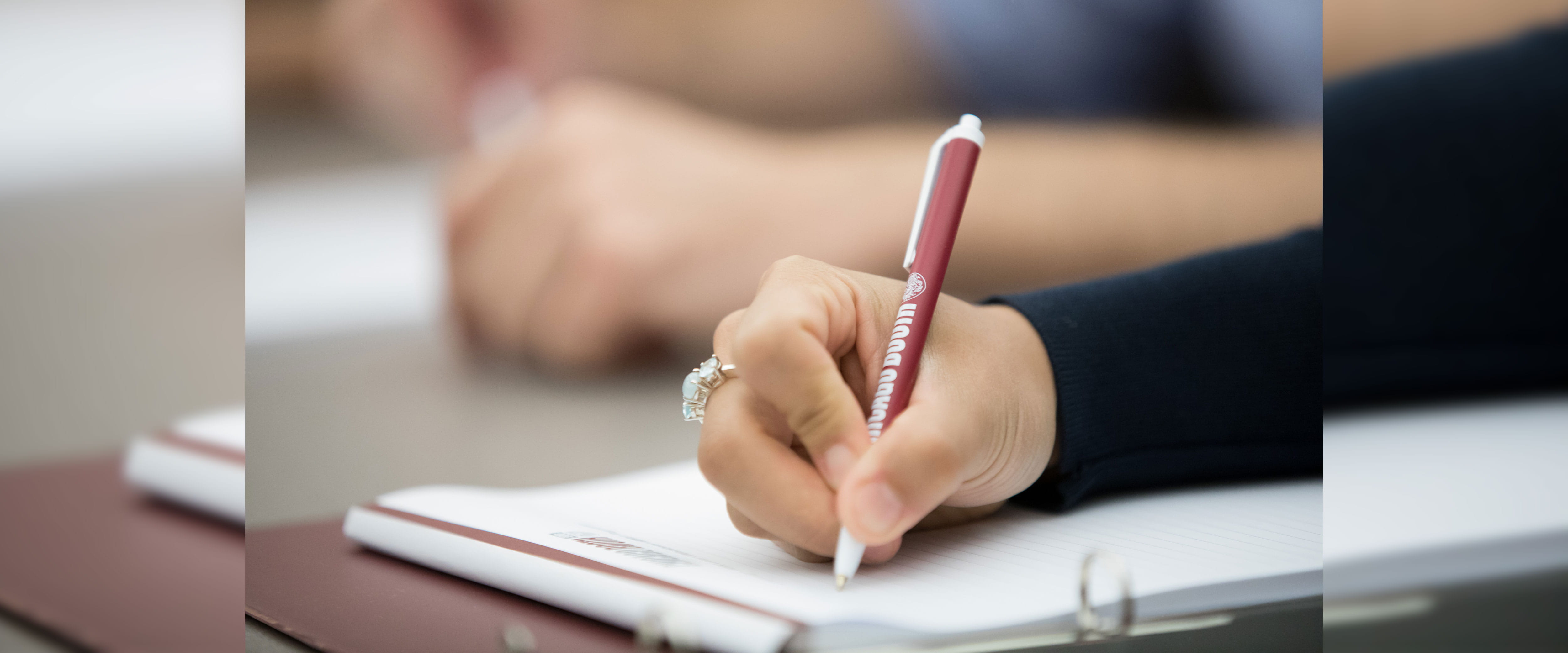 hand of individual with Booth pen writing on notepad