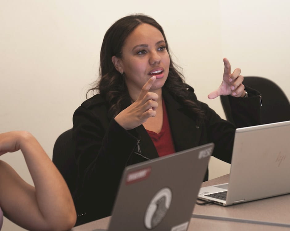 Woman sitting with laptop on table while making gesture with her hands up.
