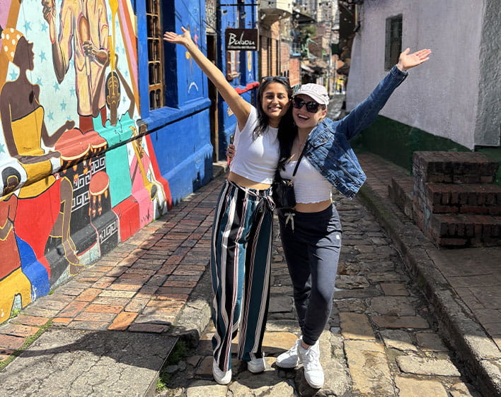 Emma and friend posing together outside with arms up smiling