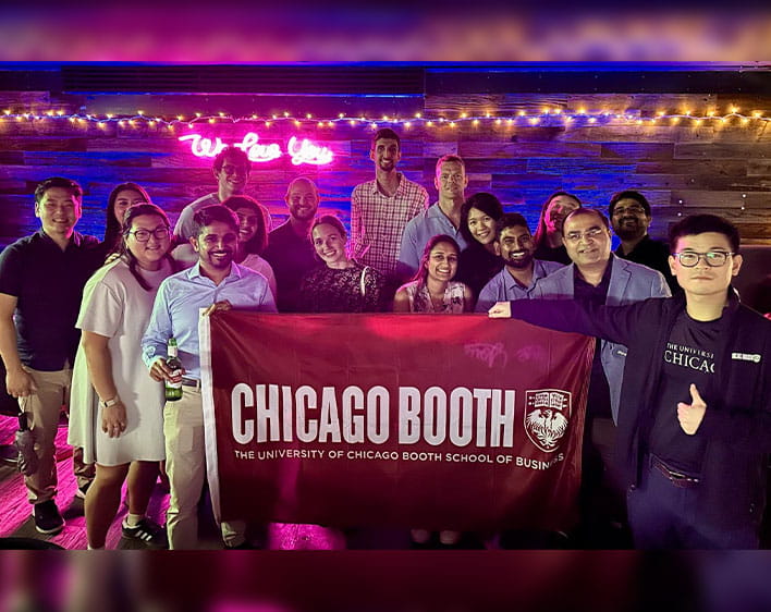 Rianna and a group of friends holding up the Chicago Booth flag