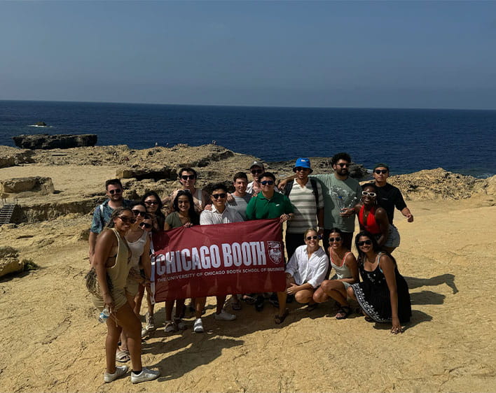 group of 15+ students at Random Walk in Malta holding up Chicago Booth flag