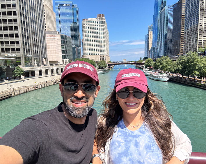 Anushka and Abhishek on boat with Chicago Booth hats on in selfie
