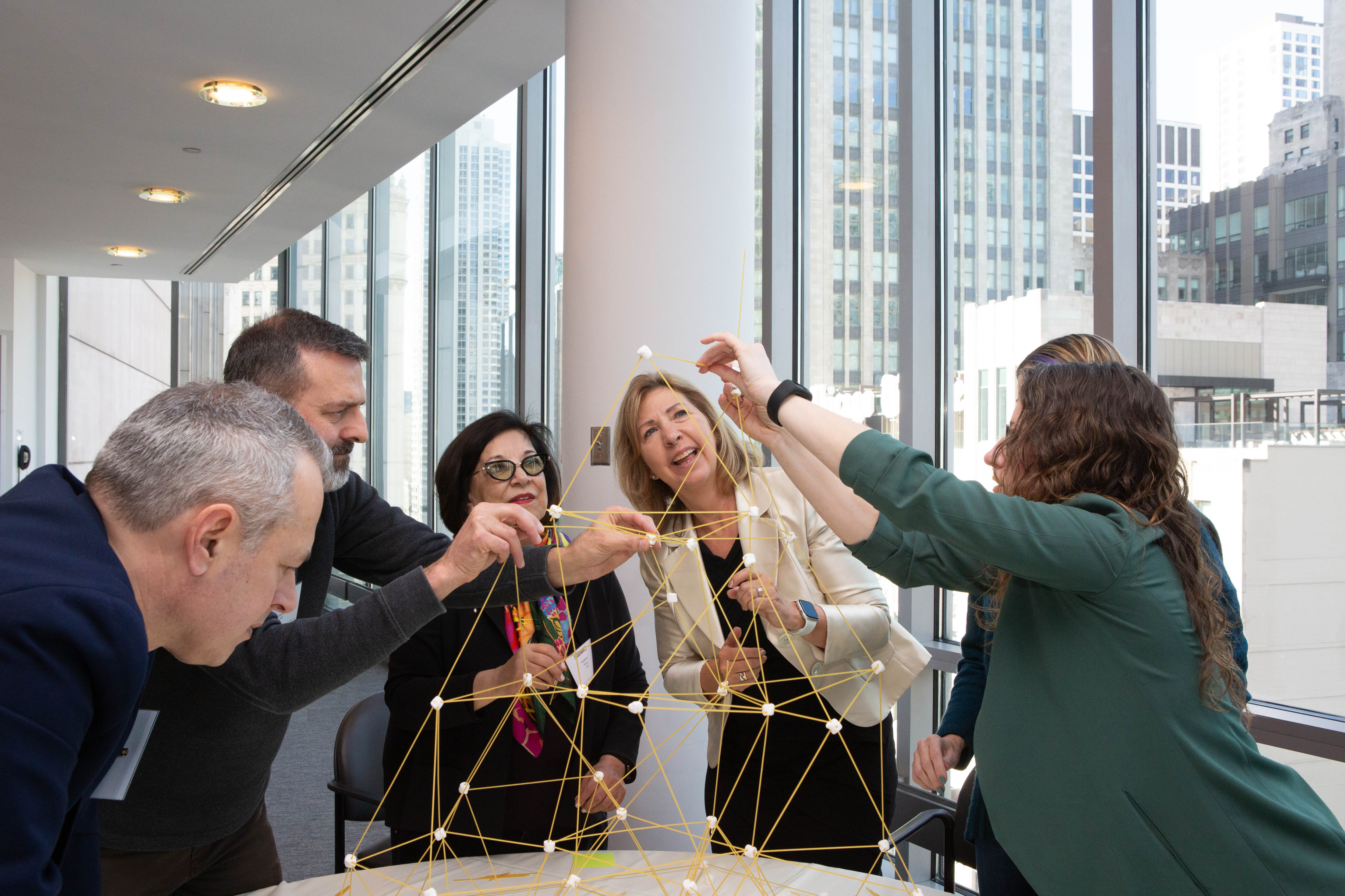 Small group of women and men constructing a tower out of marshmallows and uncooked spaghetti