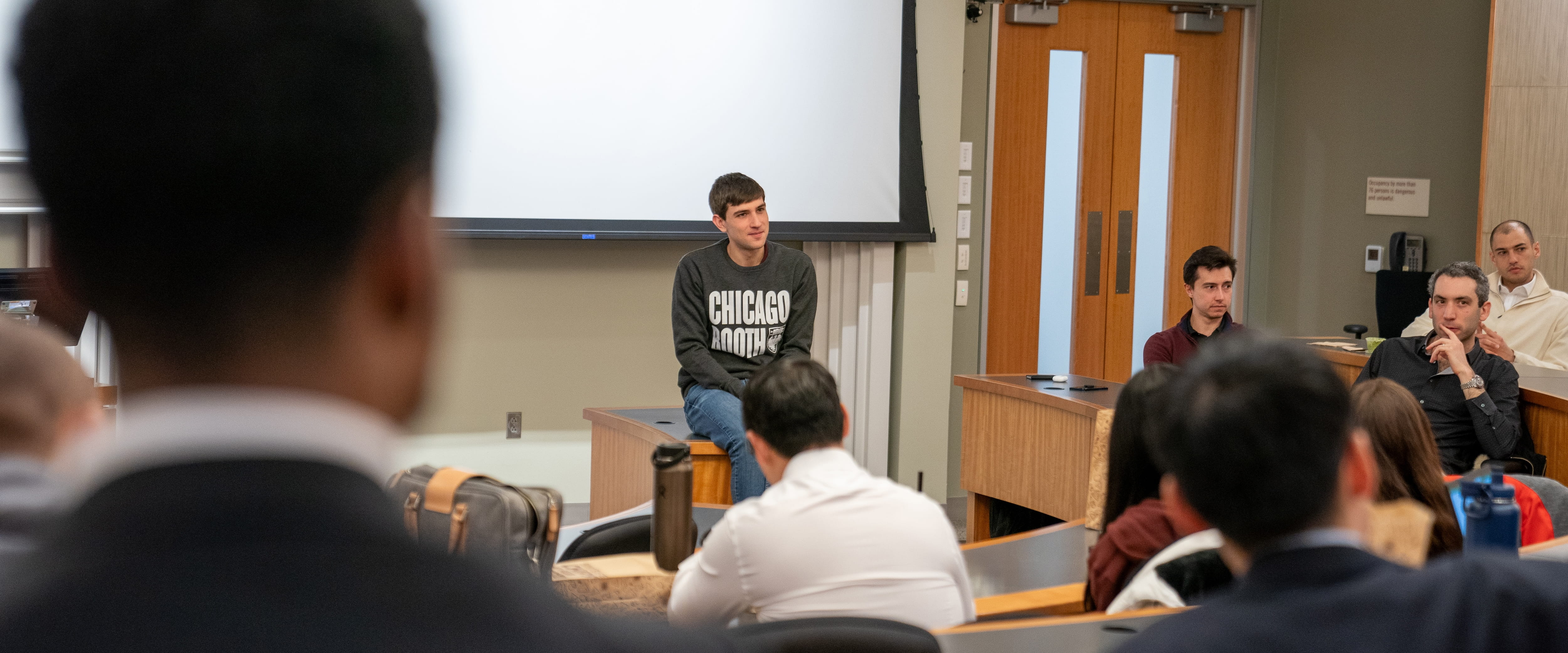 A student sitting on a desk in front of a classroom.