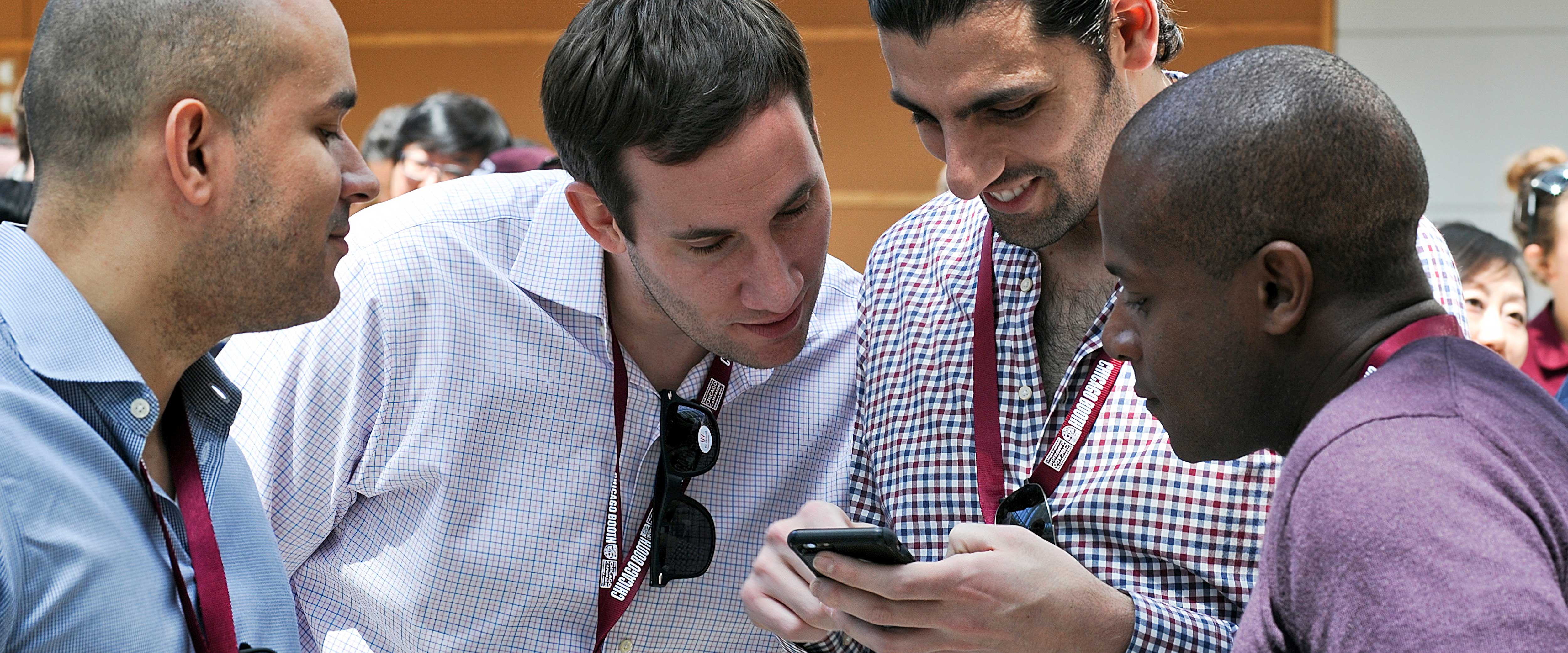 Four men in the winter garden of the Harper Center looking at a cell phone