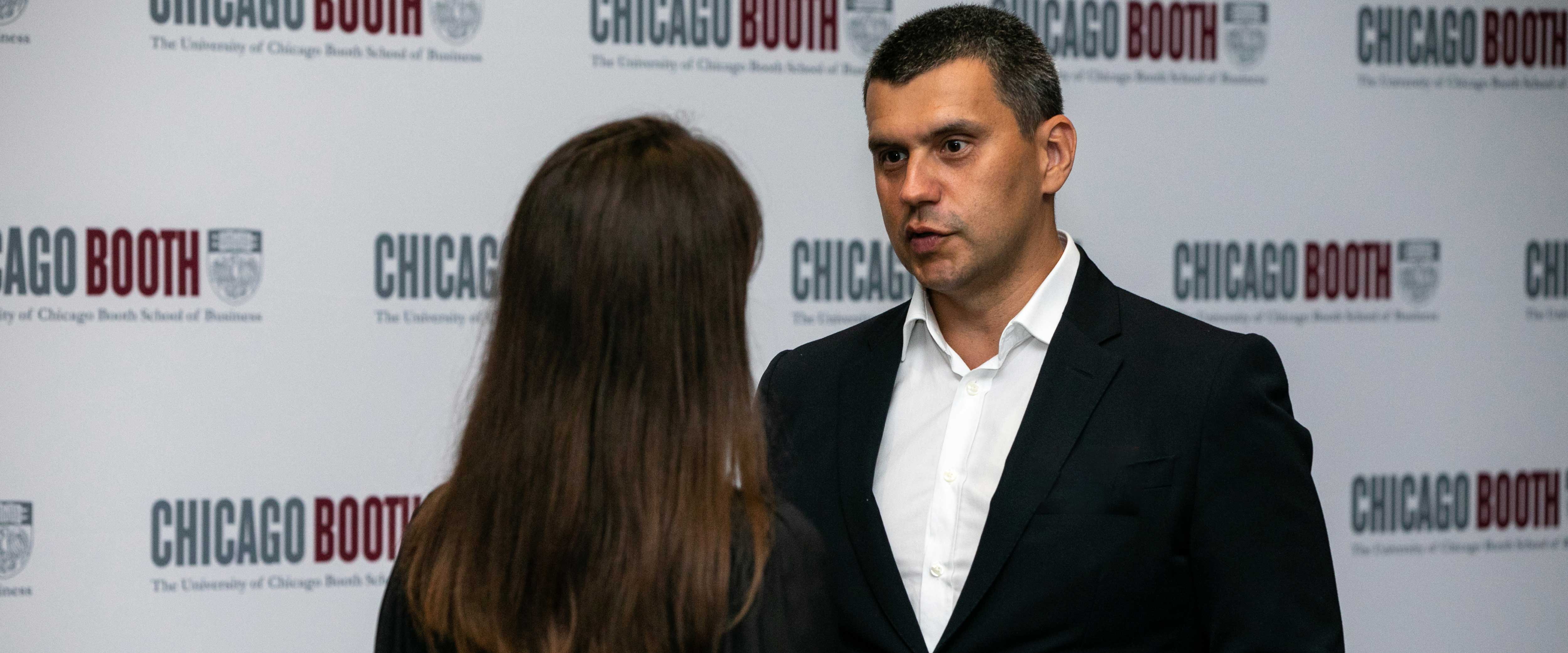 Rusian Sibaev speaking to a woman in front of a Booth banner
