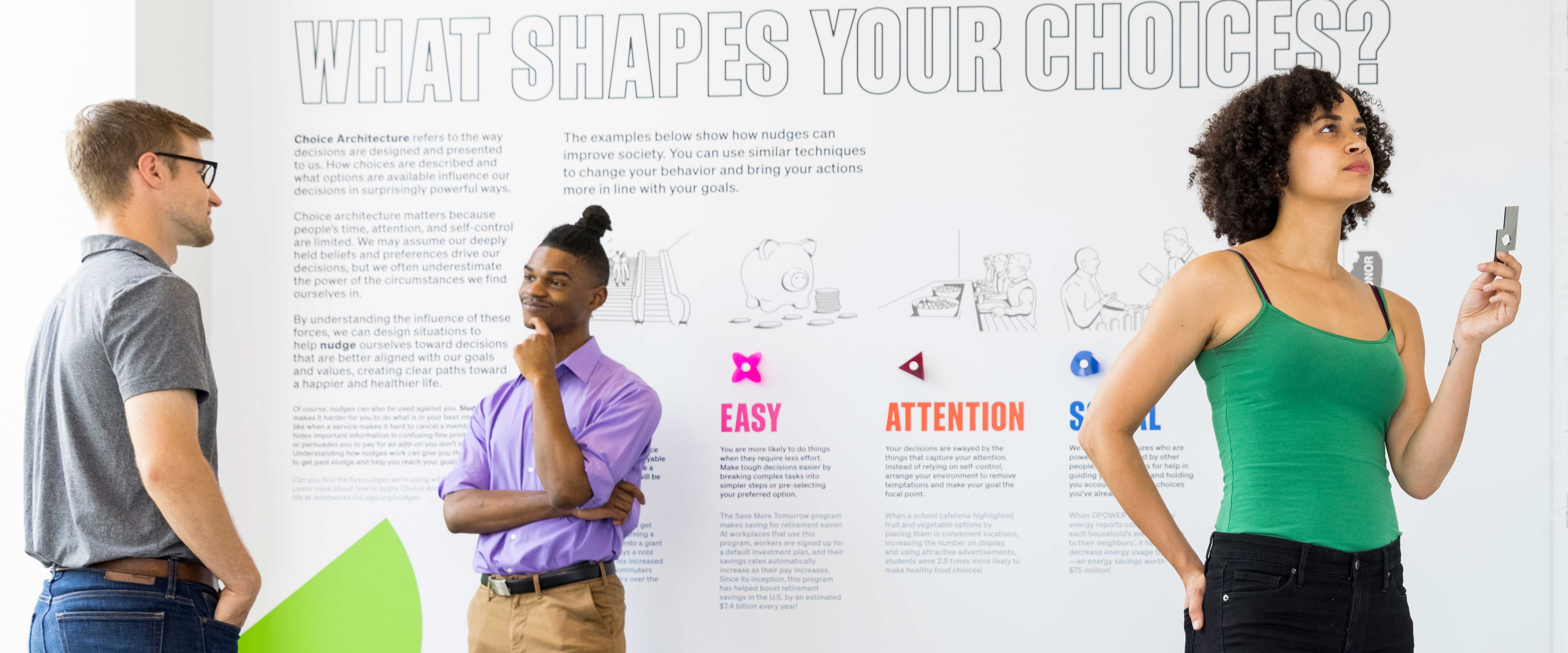 Two men talking in front of the wall and a woman adding shapes