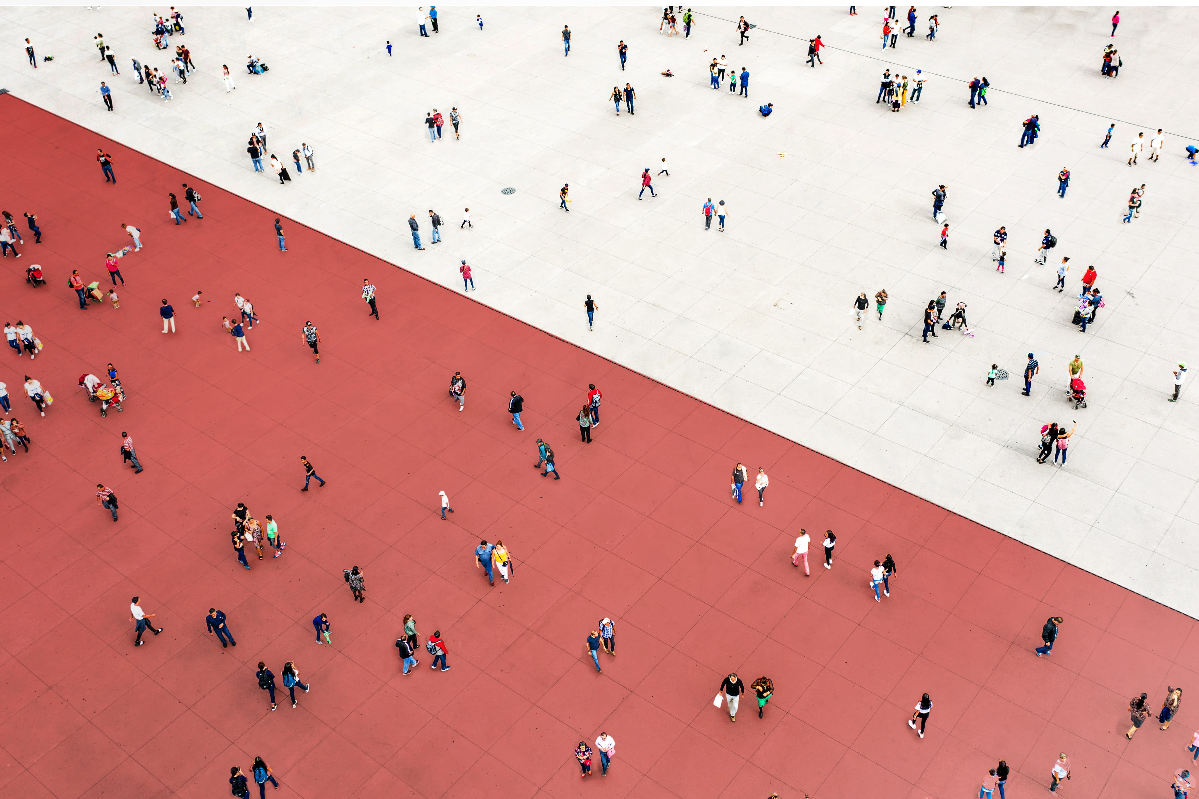 An aerial view of many people walking and standing on a sidewalk that is half rust-colored and half beige