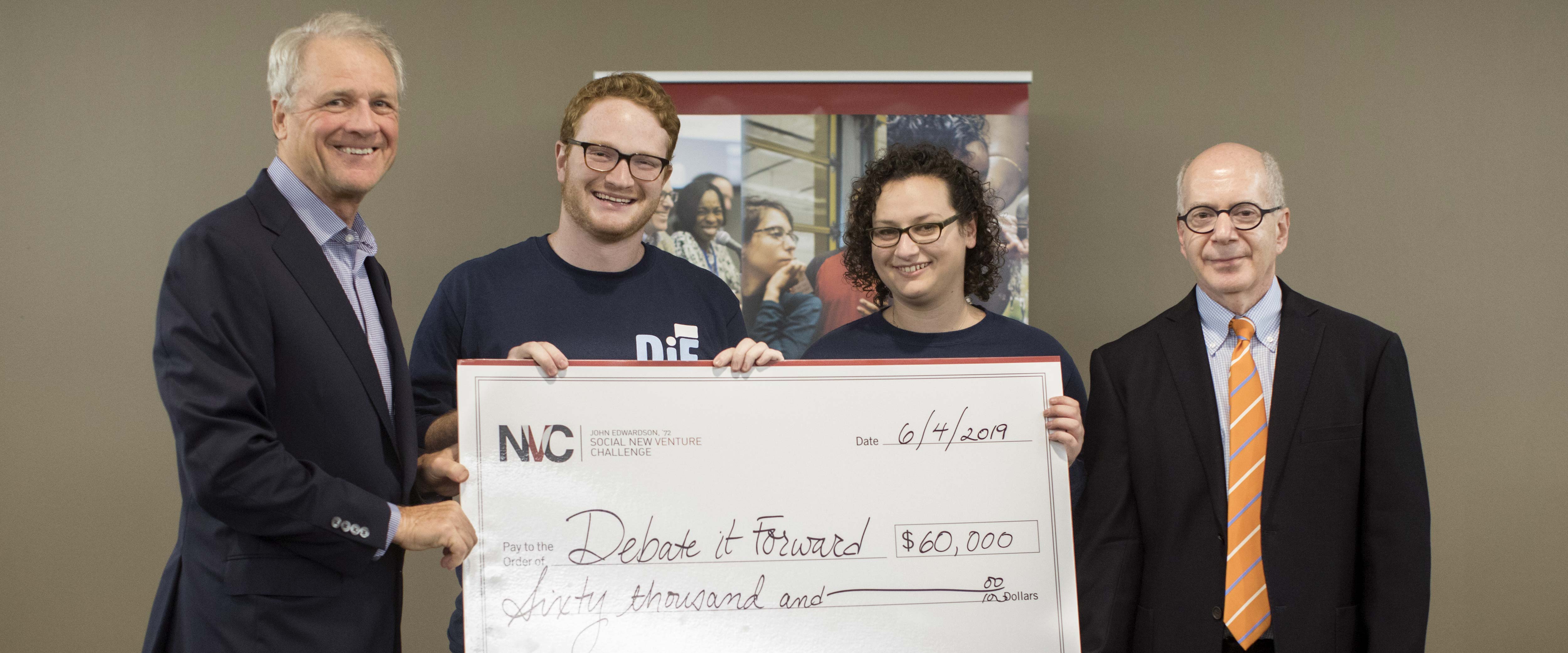 Chicago Booth SNVC 2019 winners Joshua Aaronson and Leah Shapiro of Debate It Forward pose with their giant check; John Edwardson is to their left