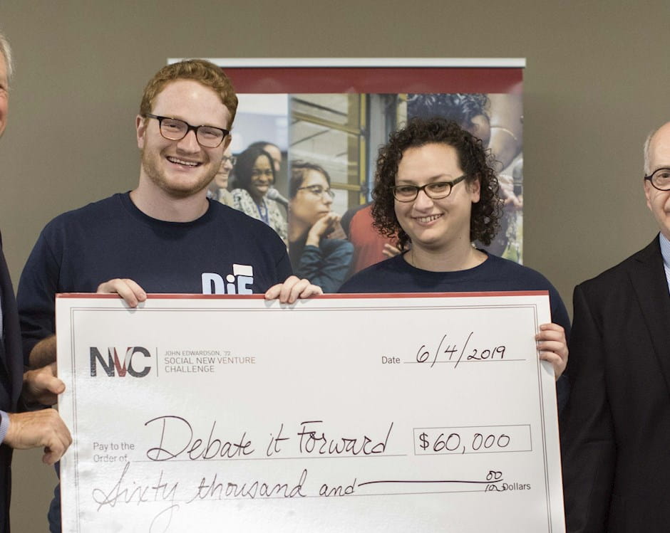 Chicago Booth SNVC 2019 winners Joshua Aaronson and Leah Shapiro of Debate It Forward pose with their giant check; John Edwardson is to their left