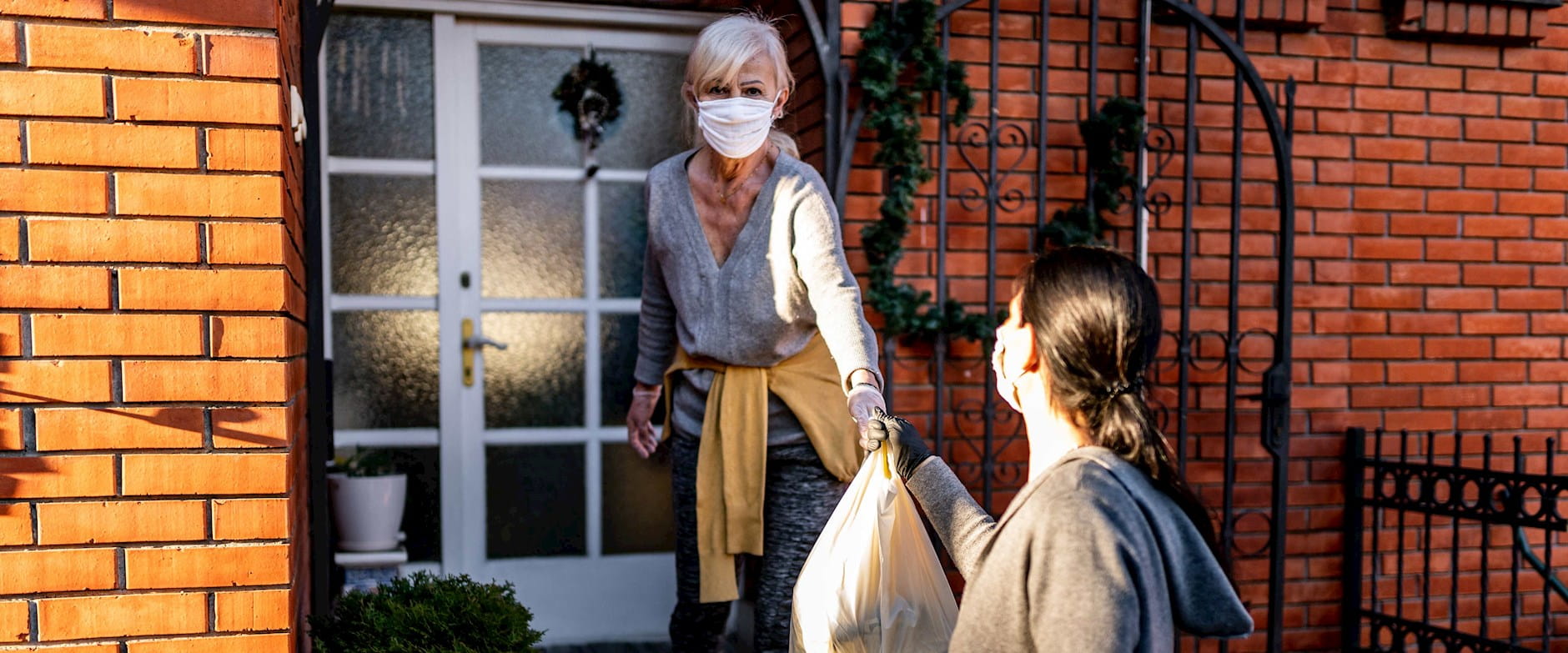 A masked volunteer hands groceries off to a masked silver-haired woman
