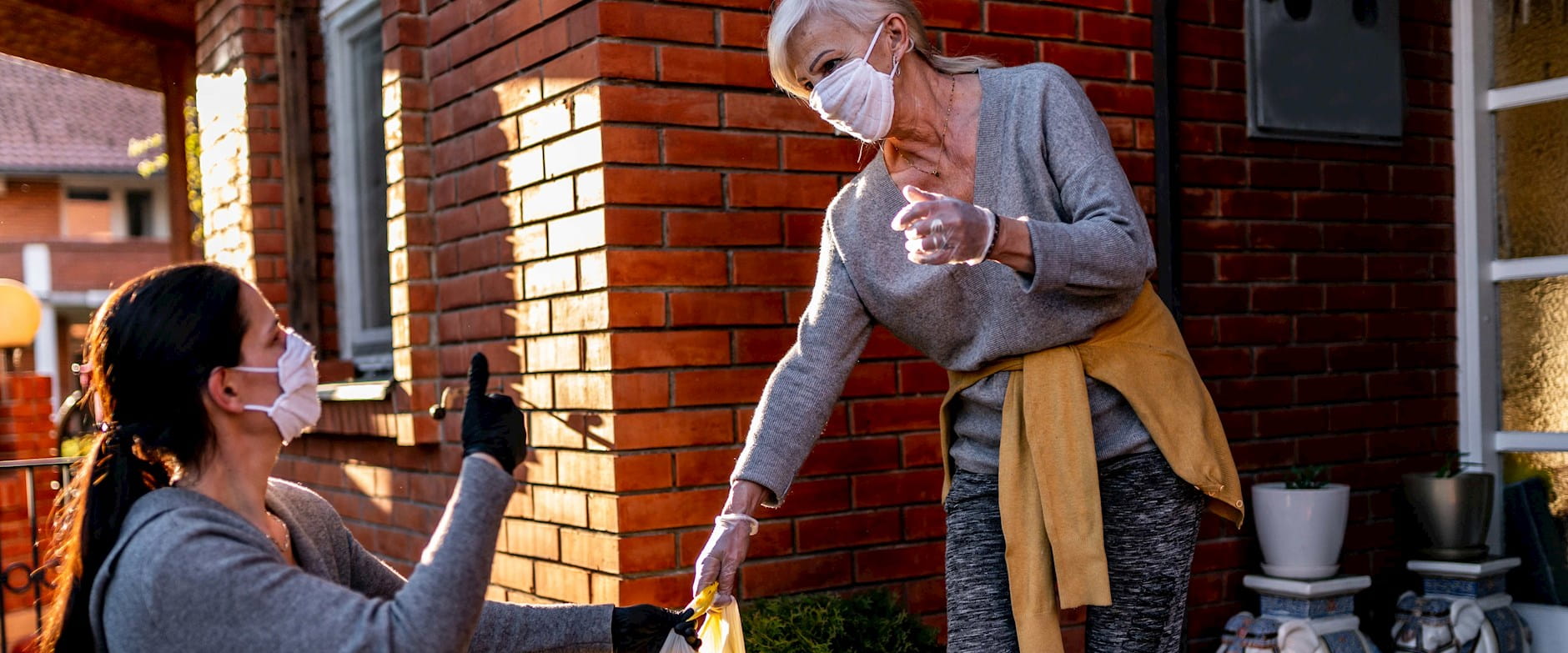 A masked volunteer hands groceries off to a silver-haired woman and gives her a thumbs-up
