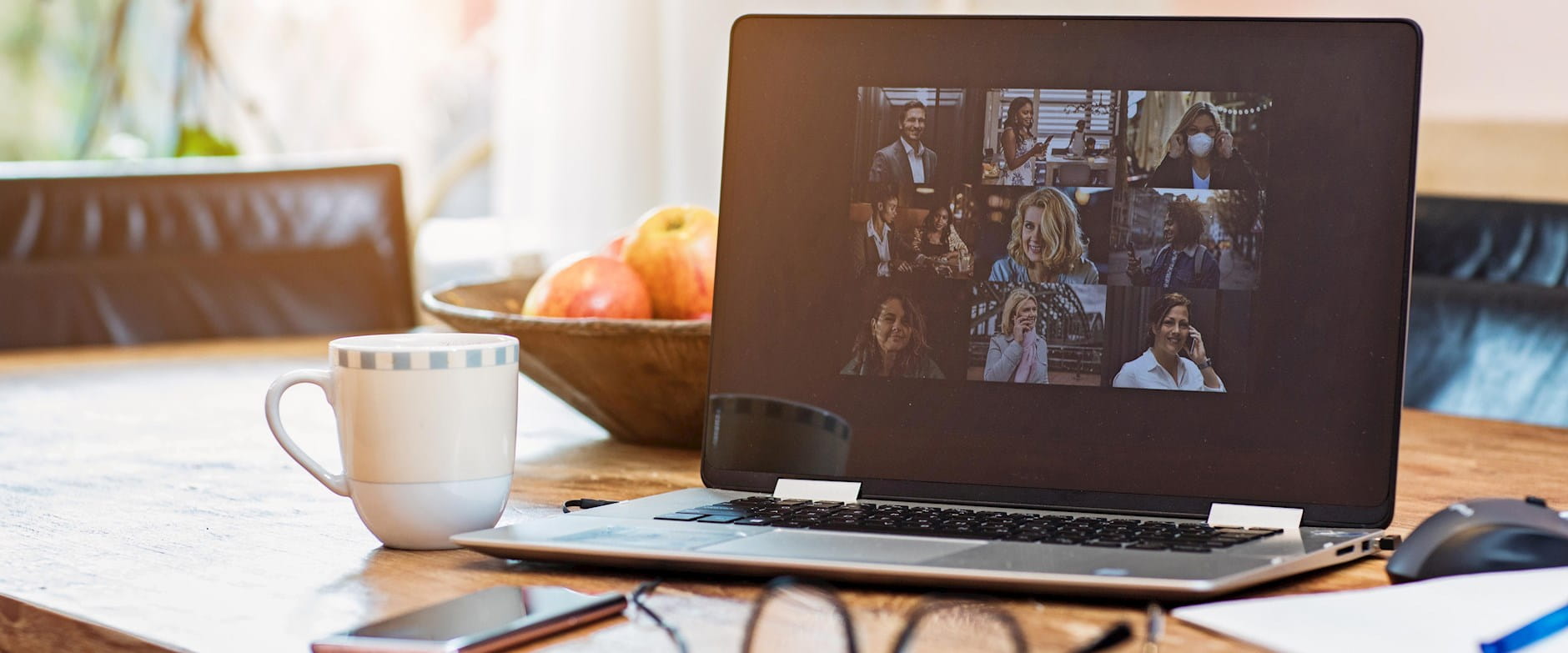 A laptop features a lively teleconference; the laptop is on a table flanked by a coffee cup