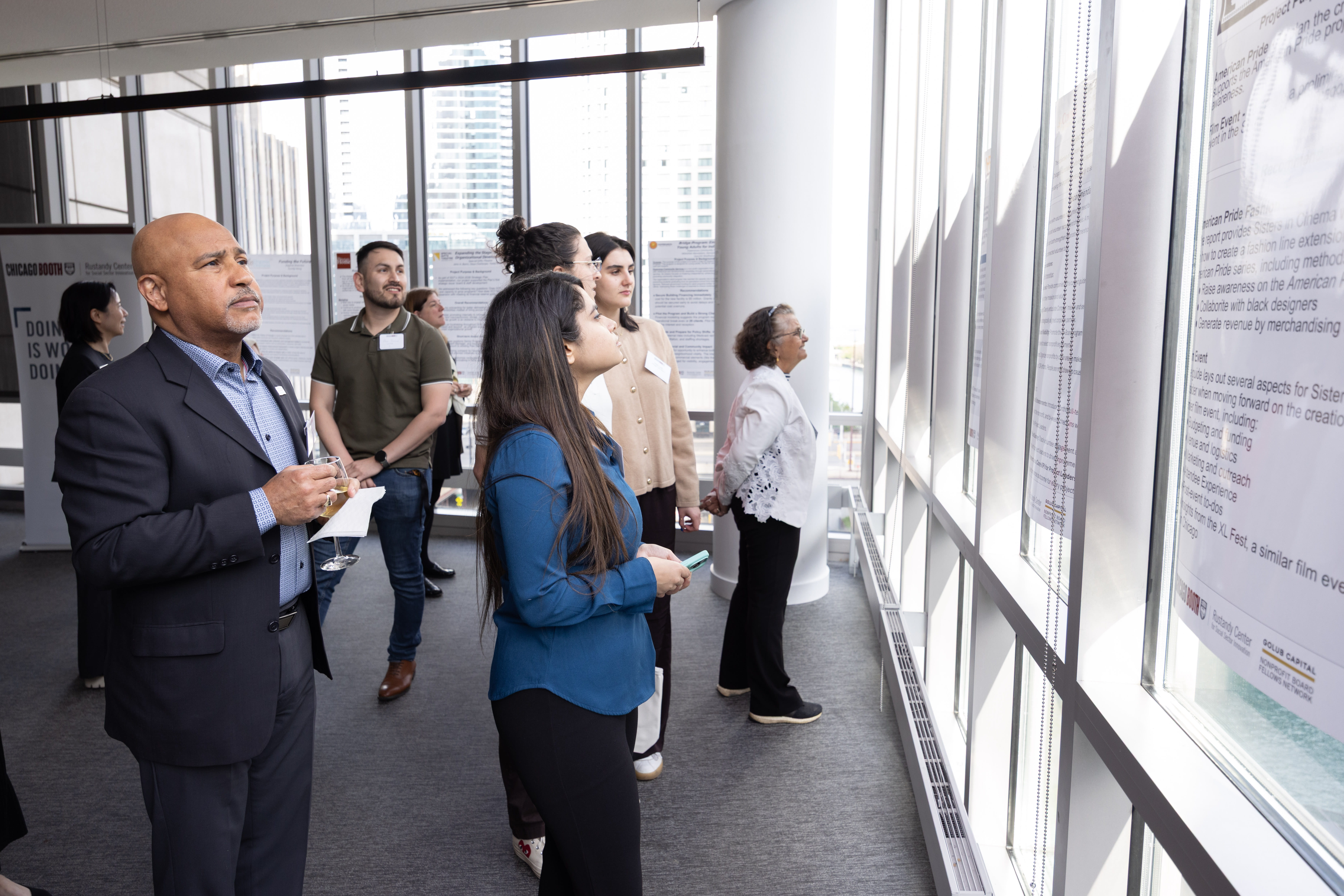 Several people standing and looking at poster presentations on a wall