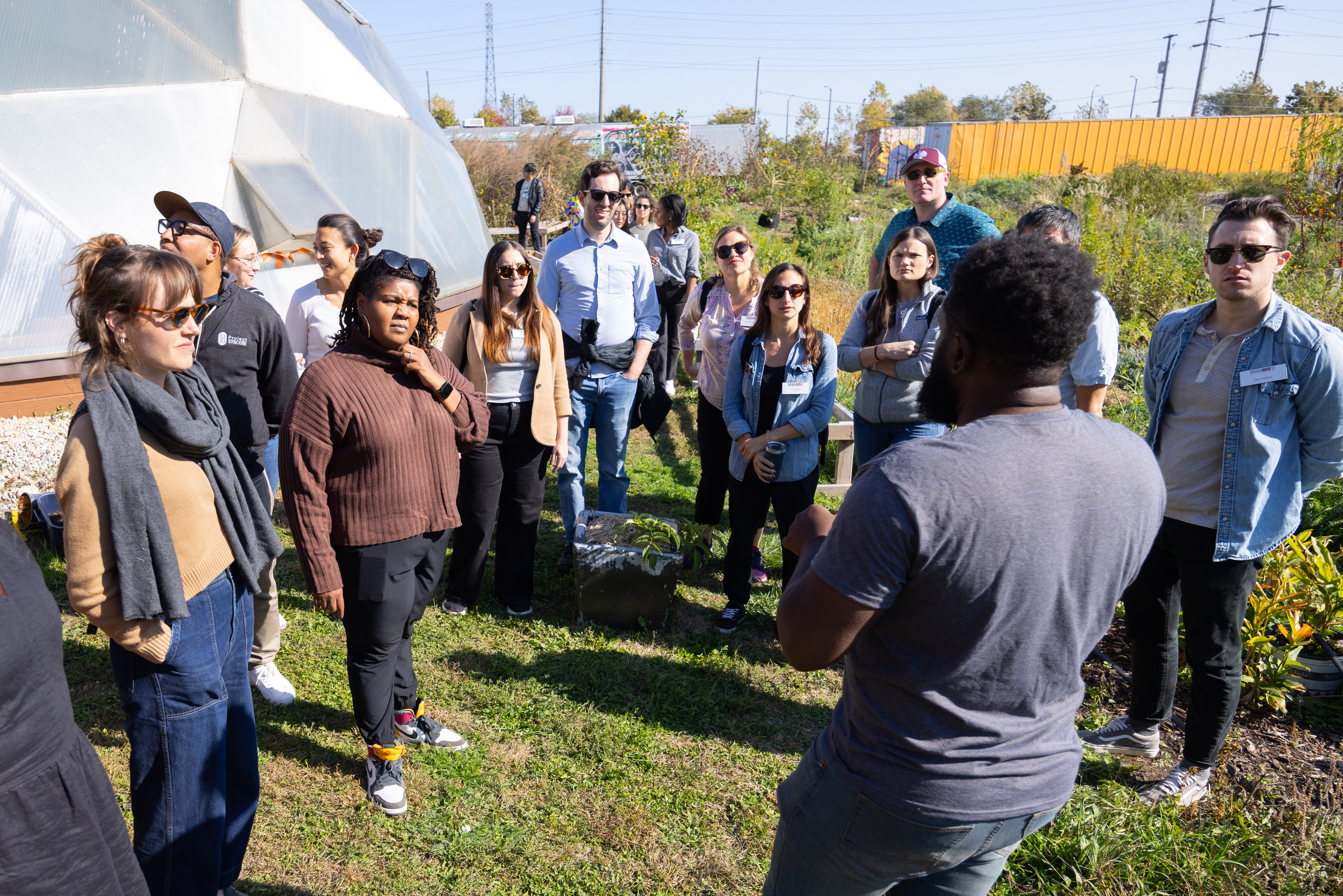 A group of people at an urban farm listening to a man with his back to the camera