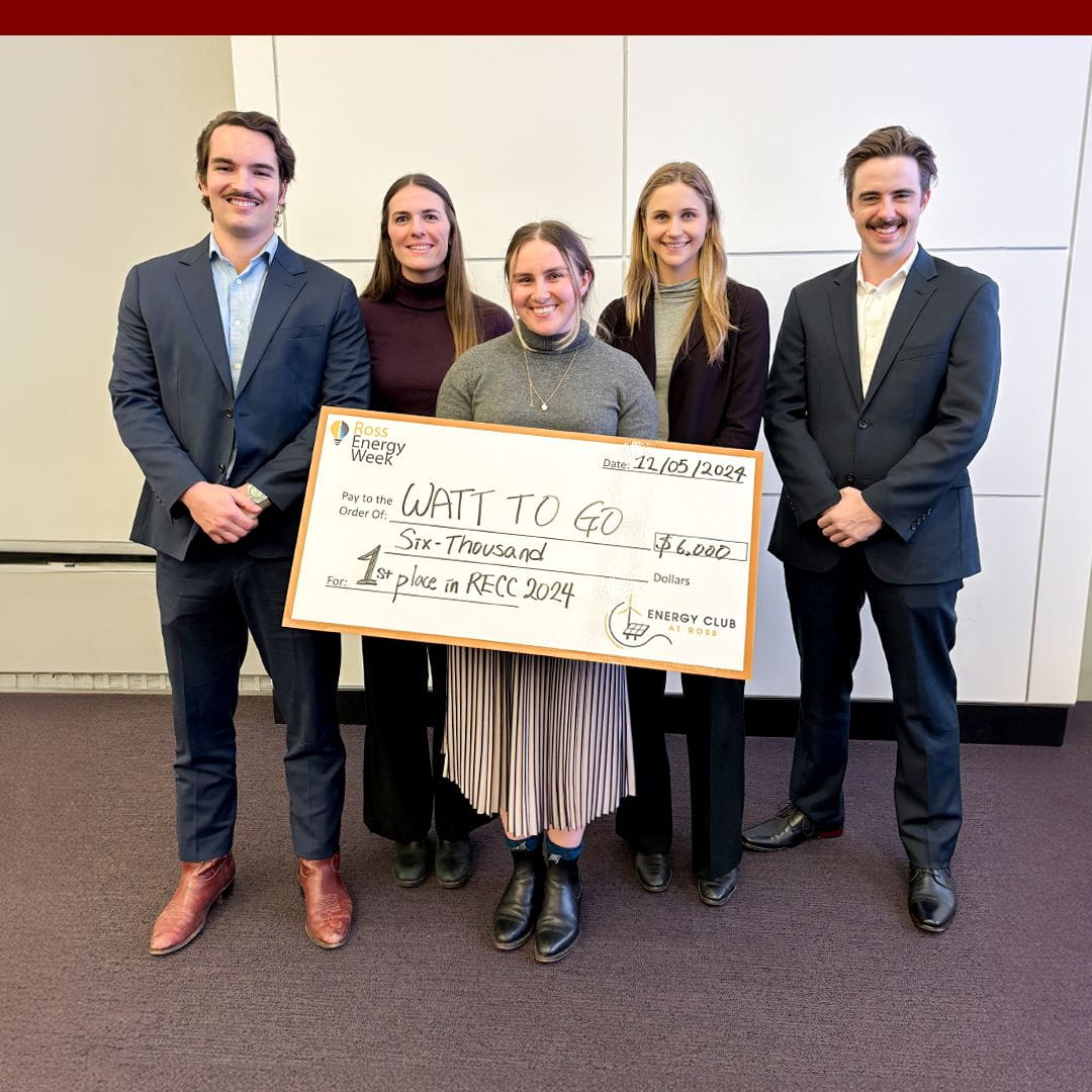 A group of five people looking at the camera, with the middle person holding up an oversized check