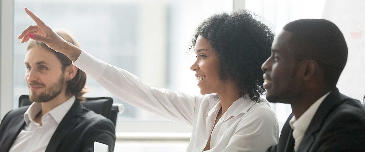 Three people smiling and looking toward the left, with one raising a hand