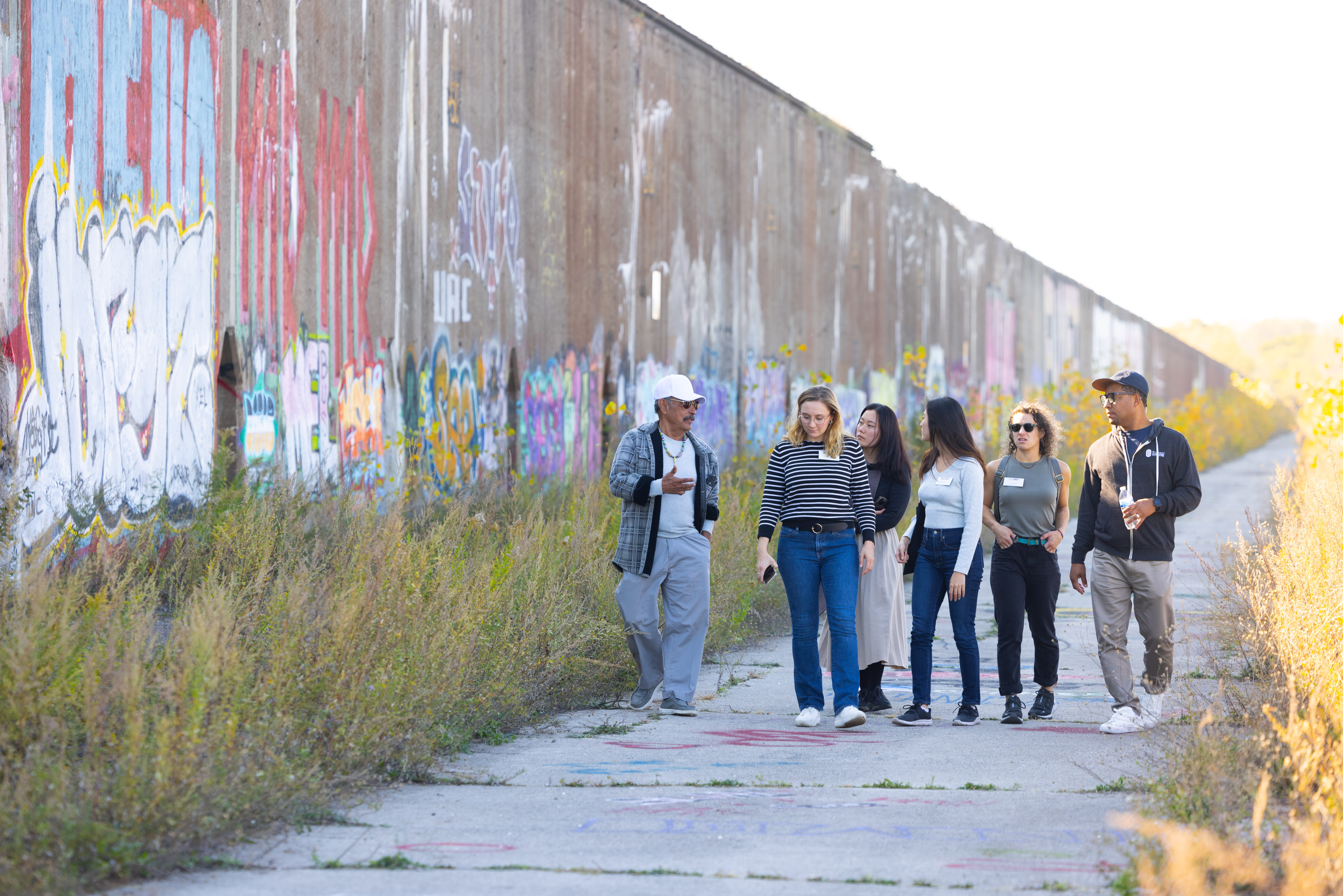 Six people walking next to a wall