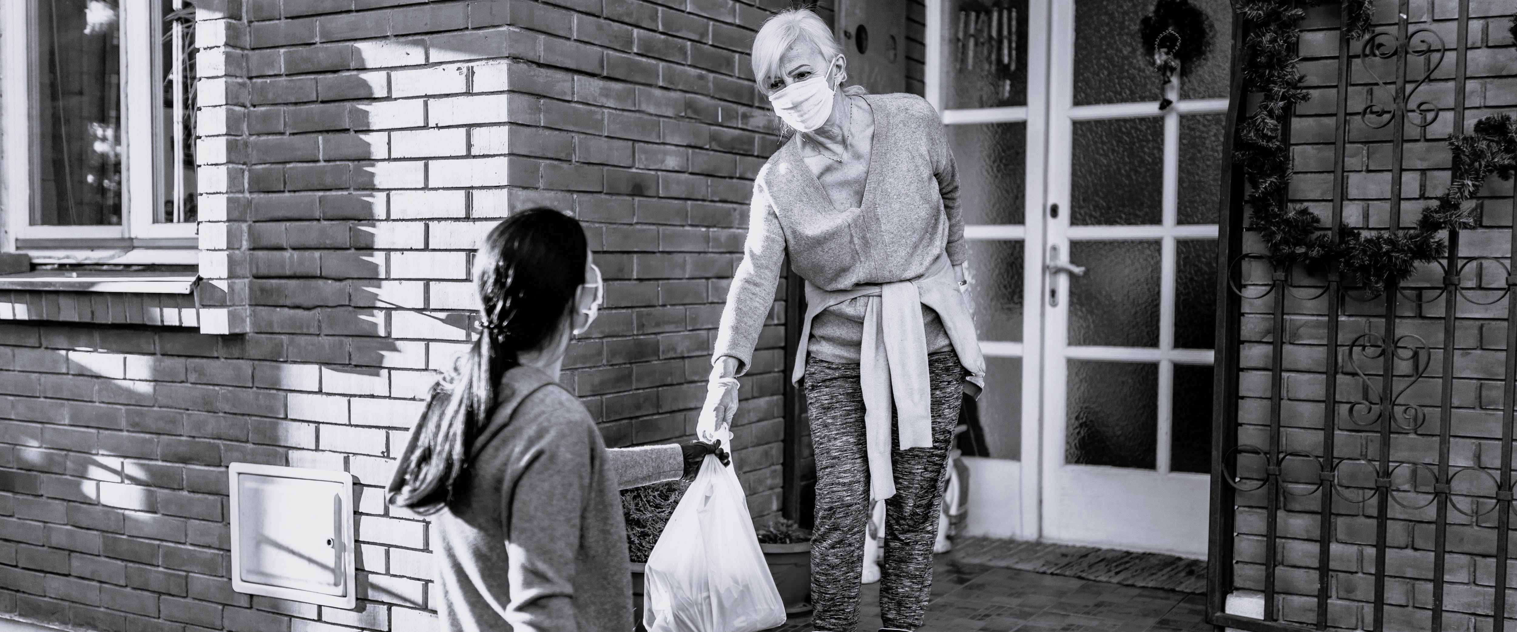 Woman handing a grocery bag to an older woman with a mask during Covid