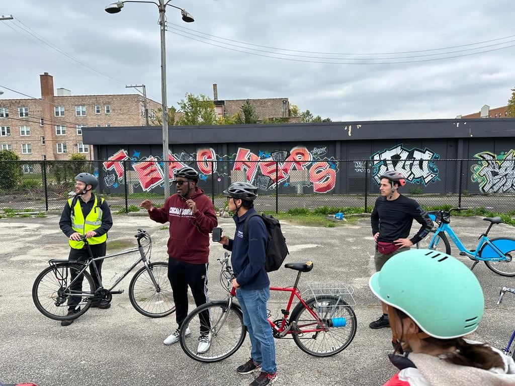 A group of people with bikes in front of a building with grafitti on it