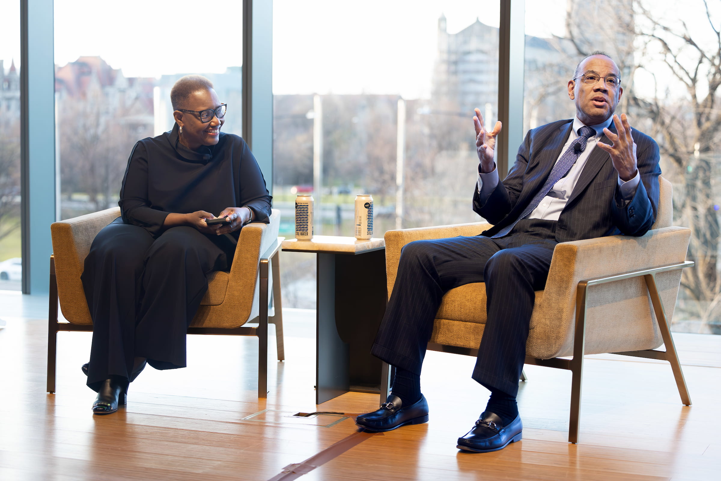 Two men sitting in chairs talking in front of a large window