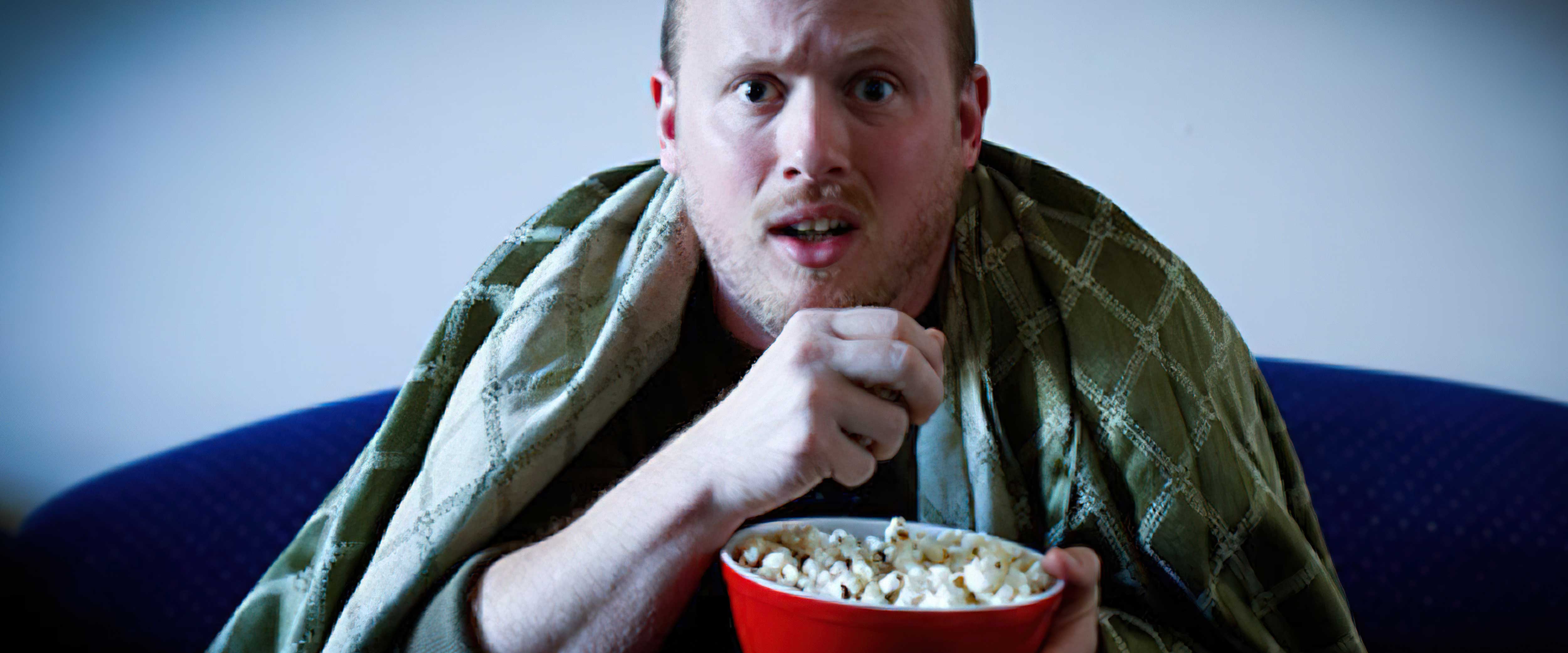 Person nervously watching TV under blanket